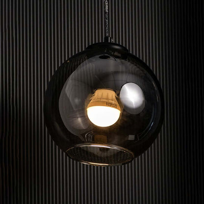 Smoked black glass globe pendant with warm glowing filament bulb highlighted on a dark background creating a dramatic stylish lighting accent.