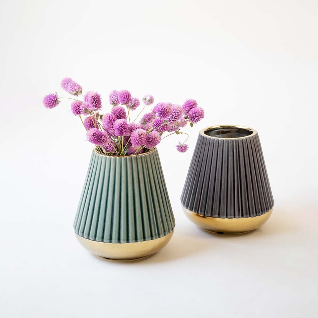 Pair of ribbed ceramic vases in contrasting shades of purple and green with golden bases displayed side by side on a wooden surface  offering a chic and contemporary home decor accent.