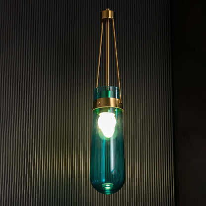 Blue glass pendant light illuminated against a black background with the light on producing a bright glow that highlights the gold frame and glass form.