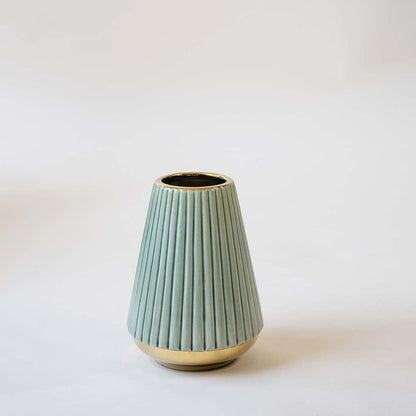 Modern green ceramic vase with vertical ribbed design and metallic gold base holding yellow artificial leaves displayed on a clean white background for a minimal aesthetic.
