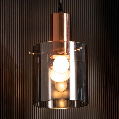 A contemporary copper and smoky glass pendant light glowing warmly against a dark textured background creating a rich ambient lighting effect.
