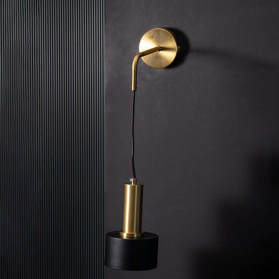 Sleek unlit wall lamp with brass mount and black cylinder spotlight shown on black background showcasing premium metal finish quality.
