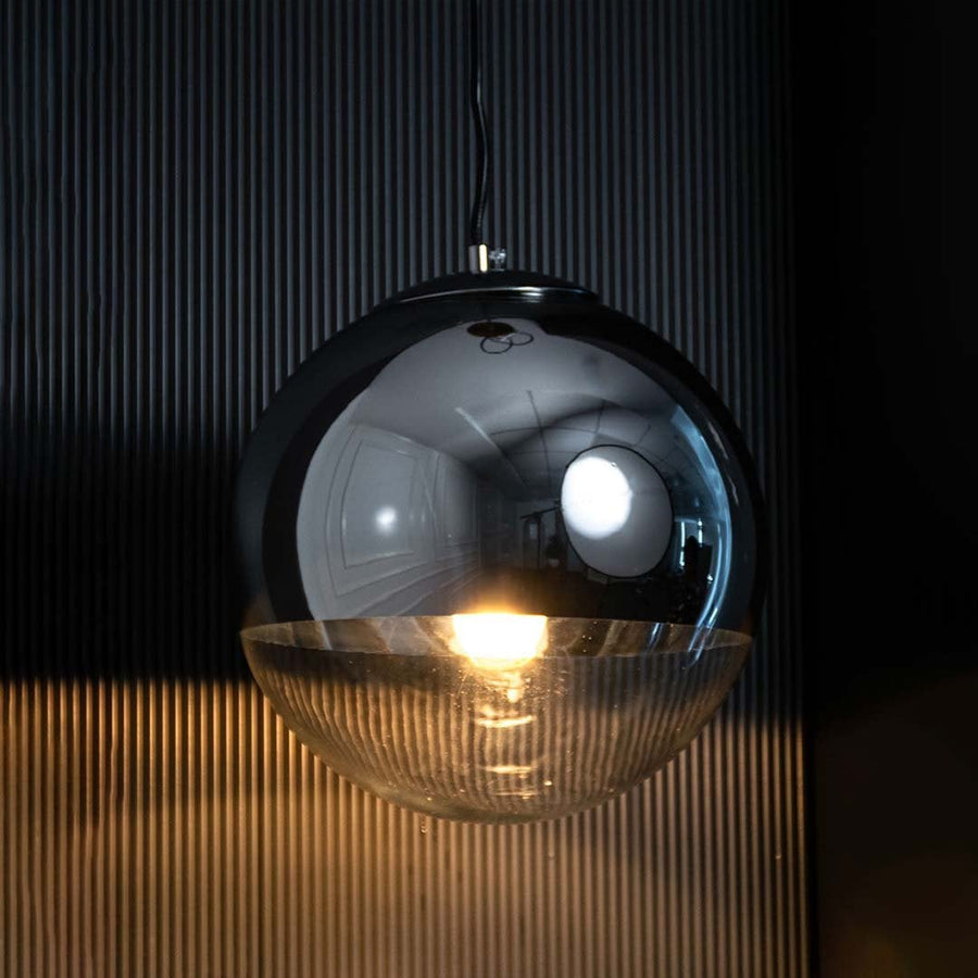 A modern smoked glass globe pendant light glowing warmly against a dark background creating a rich ambient lighting effect for premium interior decor.