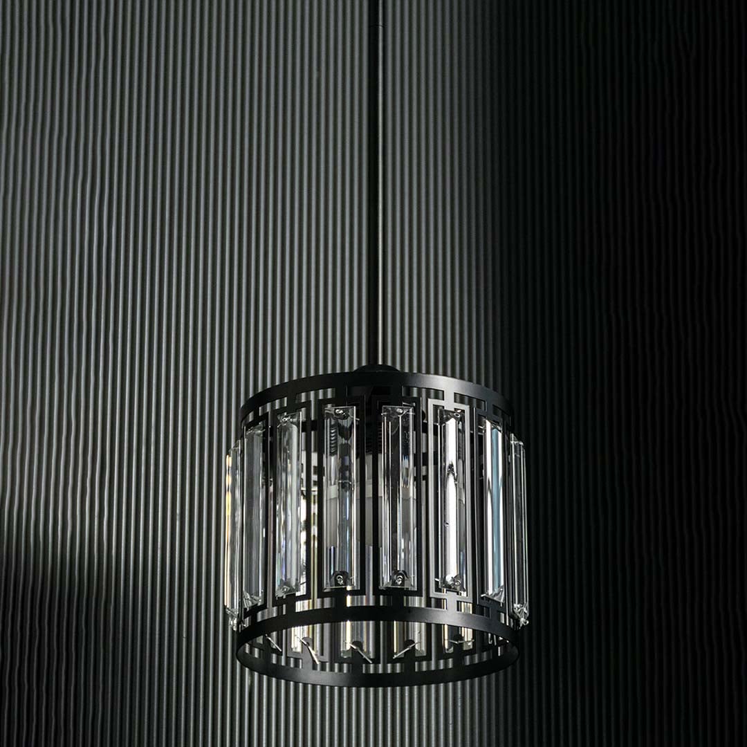 Crystal and metal pendant light with bulbs off shown on a dark background highlighting its bold black frame and clear crystal inserts.