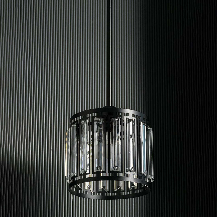 Crystal and metal pendant light with bulbs off shown on a dark background highlighting its bold black frame and clear crystal inserts.