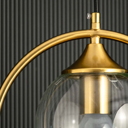A detailed closeup of a gold ring pendant light showing the smooth metallic finish and clear glass globe with subtle reflections highlighting the craftsmanship.
