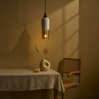 Modern white and amber glass pendant light hanging above a dining table with a cane chair and ceramic vase for a minimalist home decor look.