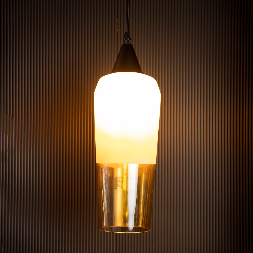 Glowing amber glass and white metal pendant lamp turned on suspended against a dark black background highlighting the warm light emission.
