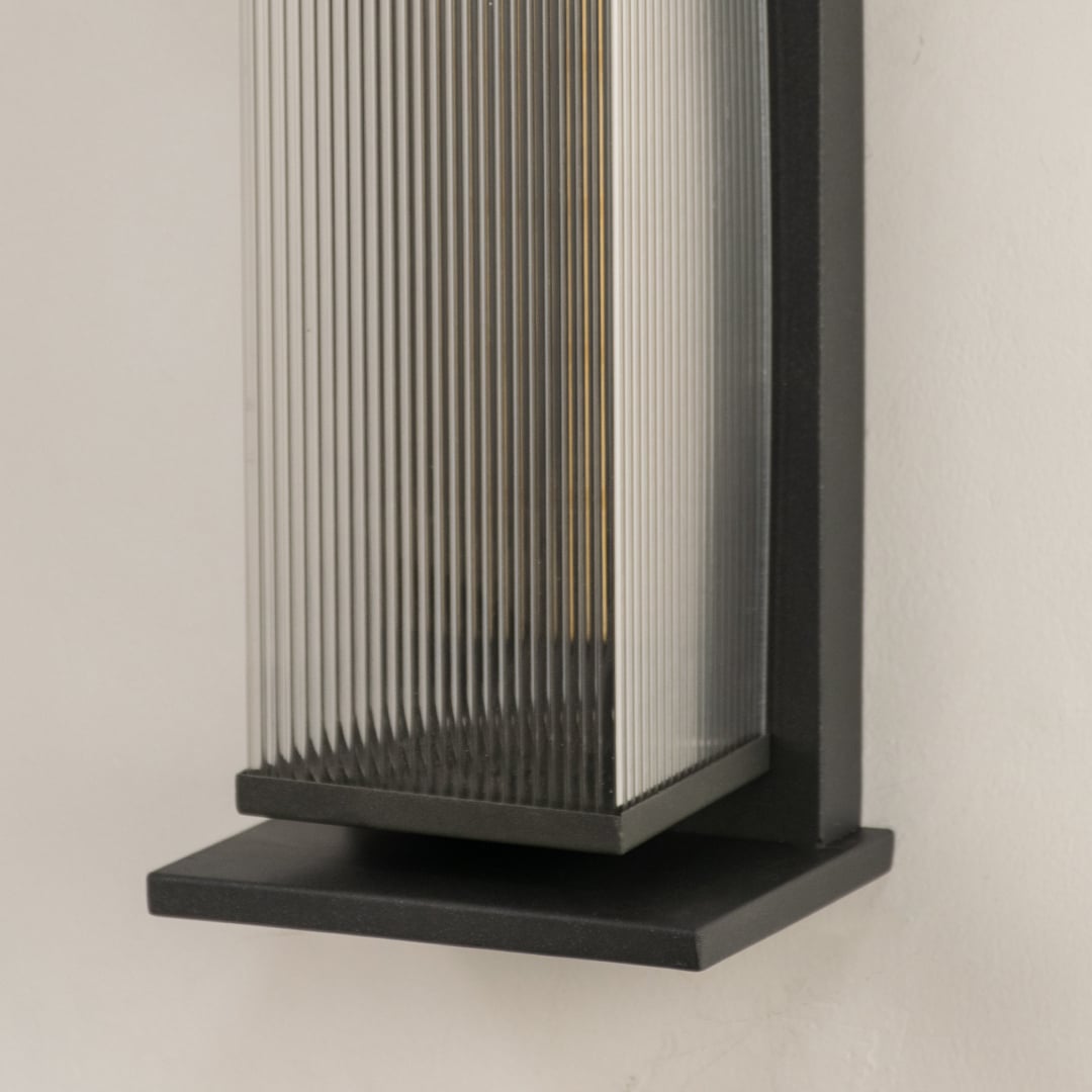 Closeup view of matte black metal frame and vertical ribbed glass texture of the modern outdoor wall lighting fixture detail.