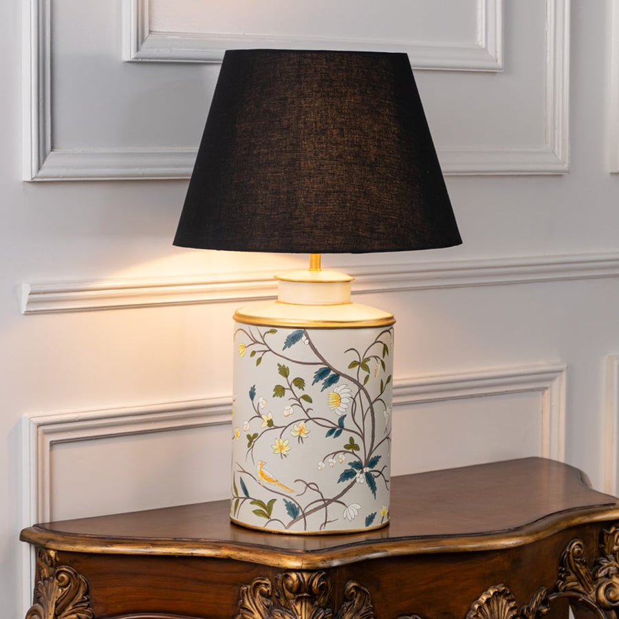 Classic ceramic table lamp with hand painted floral design and black shade styled on wooden table for cozy ambient bedroom or living space.