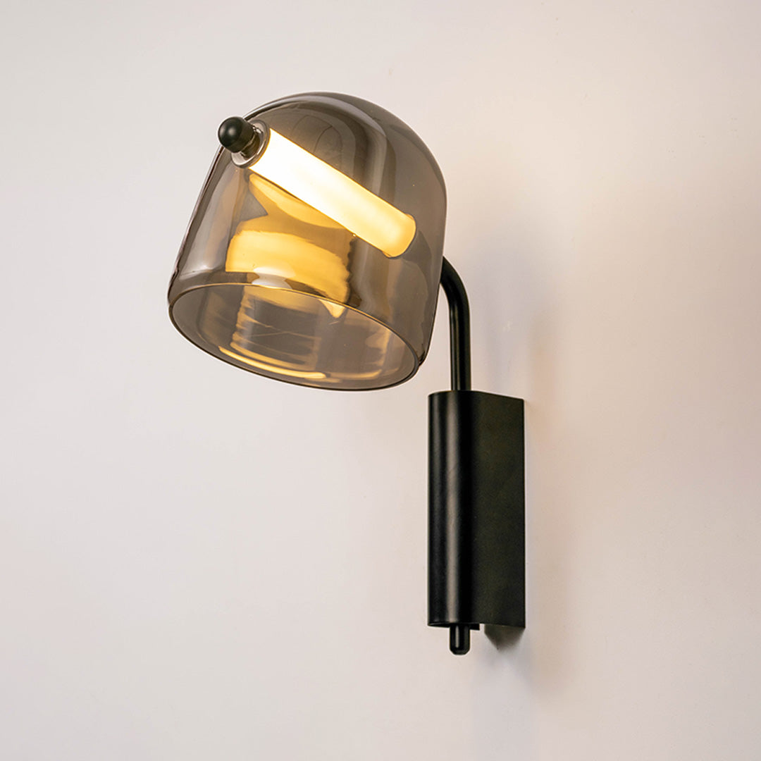 Stylish tinted glass wall sconce with black metal frame casting warm light on neutral wall background perfect for modern interior decor lighting.
