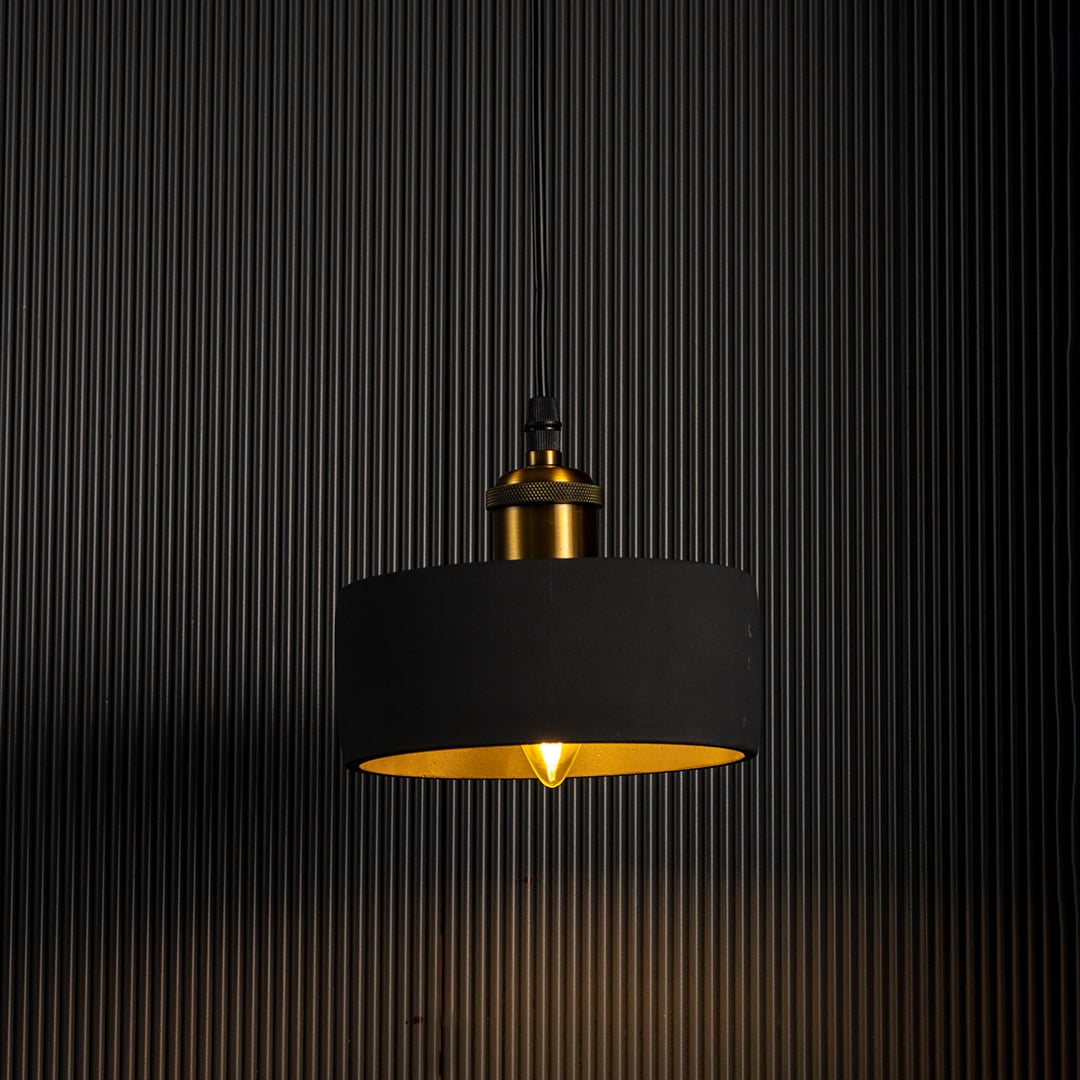 Black concrete pendant light turned on glowing warmly with brass top accent against dark background.
