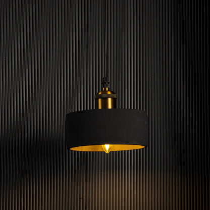 Black concrete pendant light turned on glowing warmly with brass top accent against dark background.