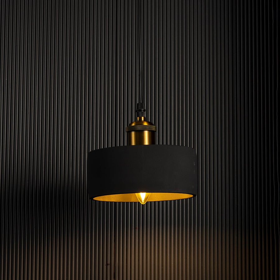 Black concrete pendant light turned on glowing warmly with brass top accent against dark background.