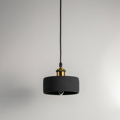 Black concrete pendant light turned off with brass top and visible bulb against white wall in modern setting.