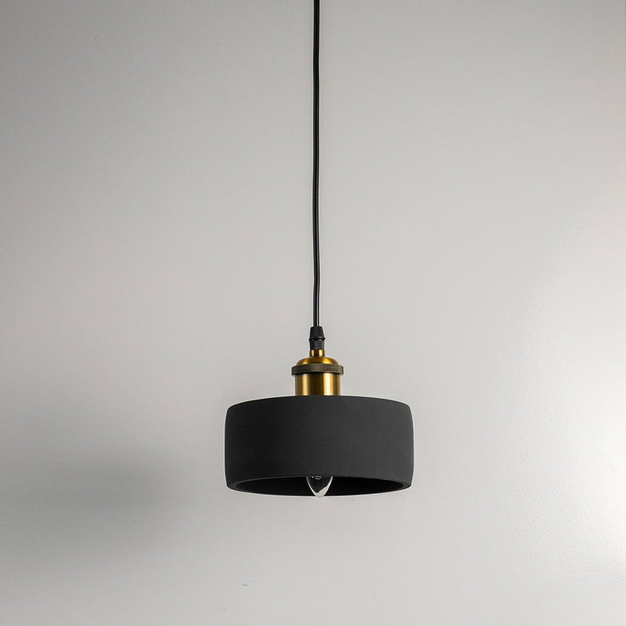 Black concrete pendant light turned off with brass top and visible bulb against white wall in modern setting.