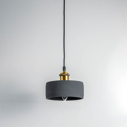 Black concrete pendant light turned off with brass top and visible bulb against white wall in modern setting.