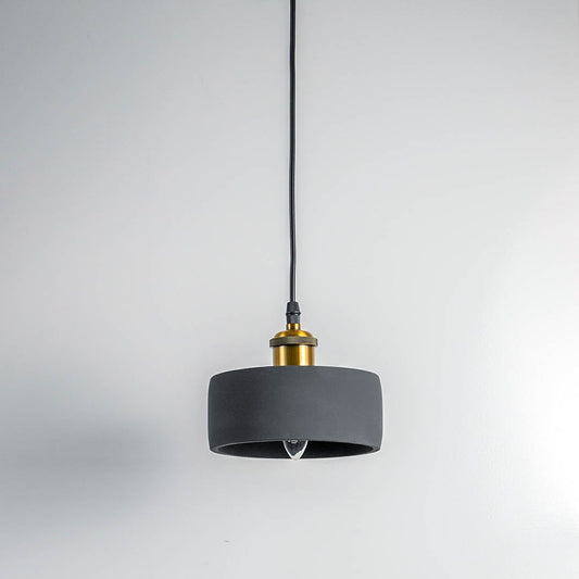 Black concrete pendant light turned off with brass top and visible bulb against white wall in modern setting.