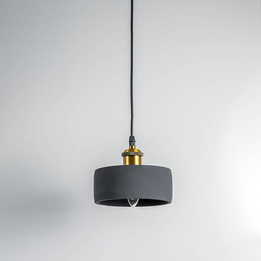 Black concrete pendant light turned off with brass top and visible bulb against white wall in modern setting.
