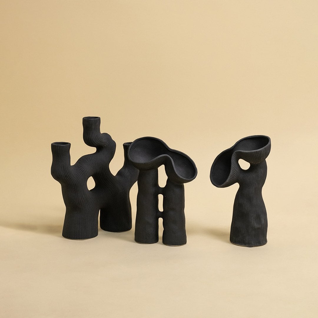 Collection of handcrafted black ceramic vases with ribbed texture and abstract form displayed on white surface.