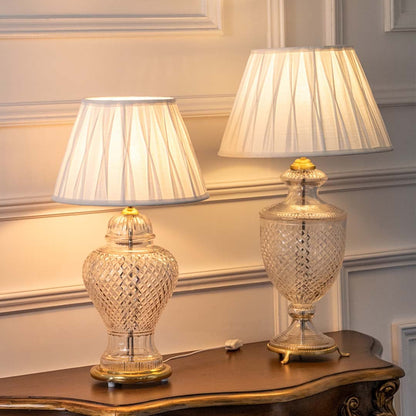 Set of two glass table lamps with pleated white shades turned on together casting soft warm light ideal for elegant bedroom or hallway decor.