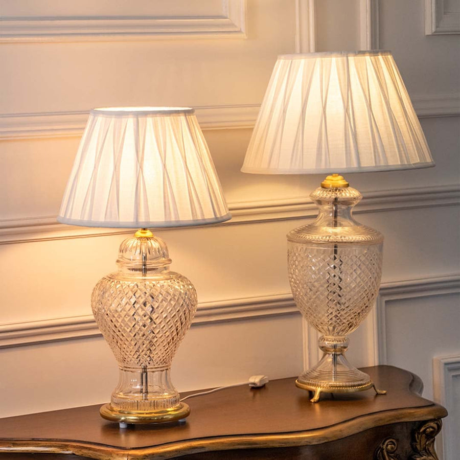 Set of two glass table lamps with pleated white shades turned on together casting soft warm light ideal for elegant bedroom or hallway decor.