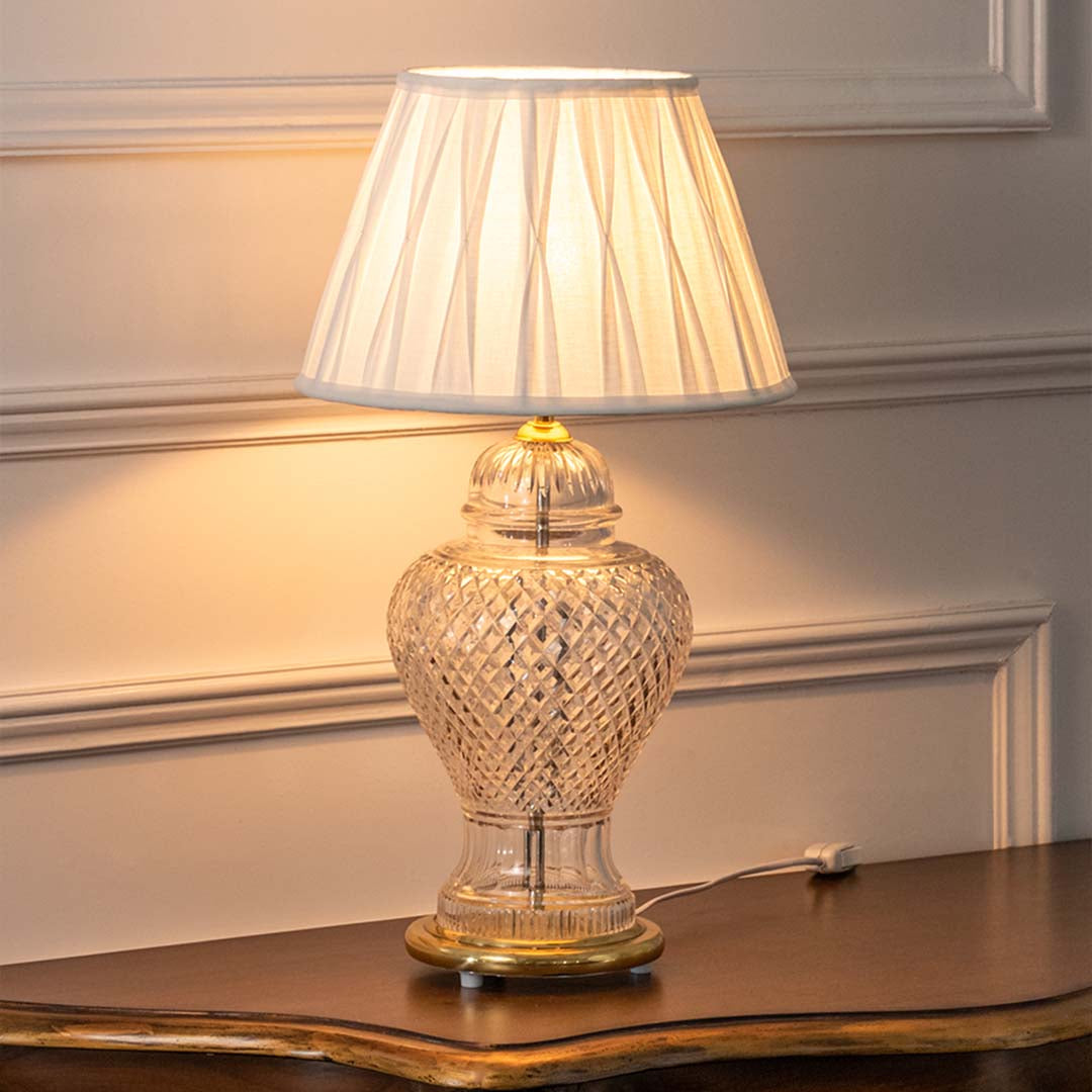 Clear textured glass table lamp with pleated fabric shade creating elegant traditional ambient lighting for interiors.