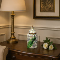 Peacock-themed decorative jar placed on a wooden console beside a gold lamp and white roses adding elegance to interior decor.