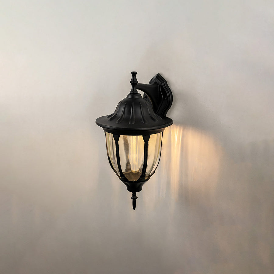 Black metal outdoor wall light on white background with clear ribbed glass shade for patio lighting decor.