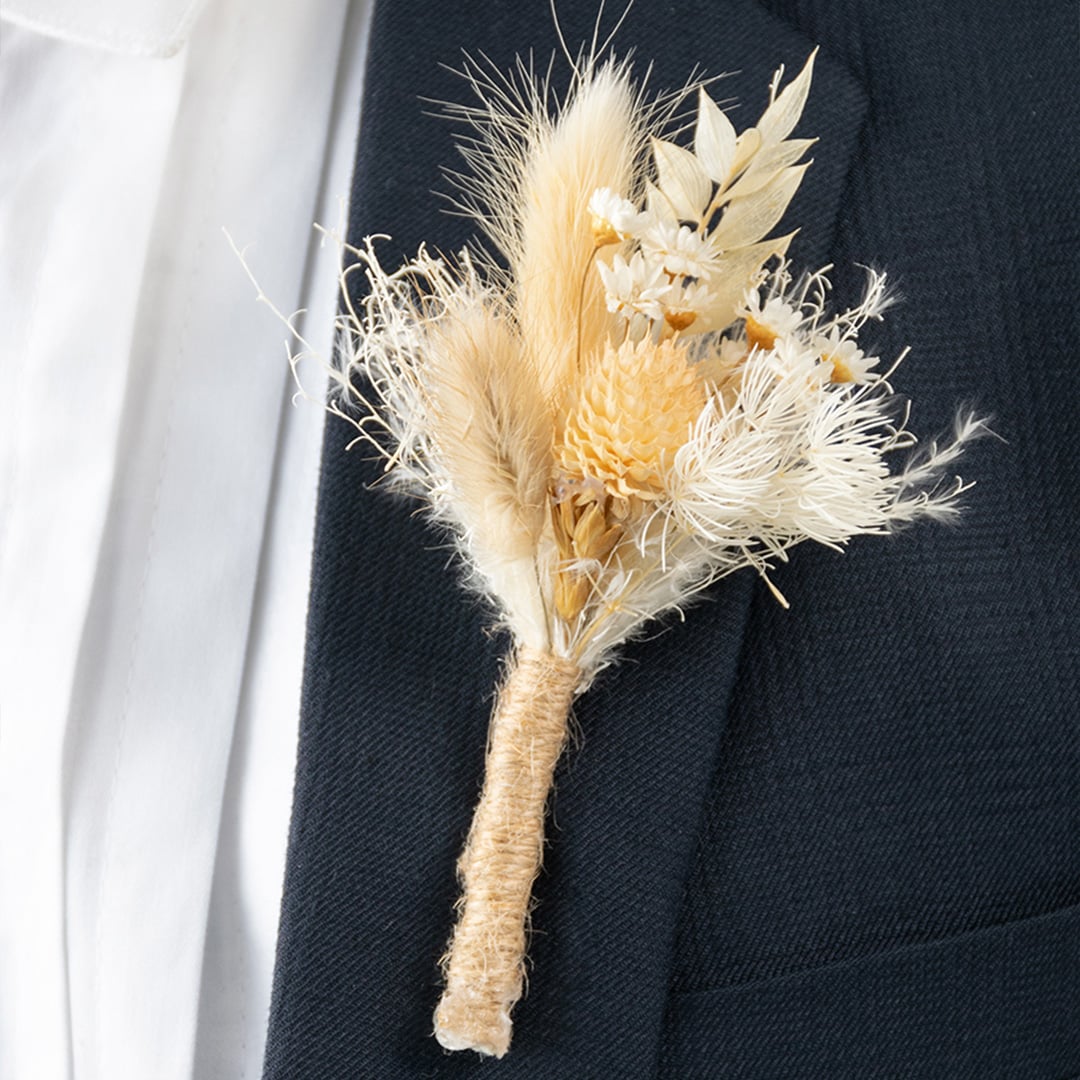 Closeup of dried flower boutonniere with natural beige stems and rustic jute wrap perfect for wedding and groom styling.
