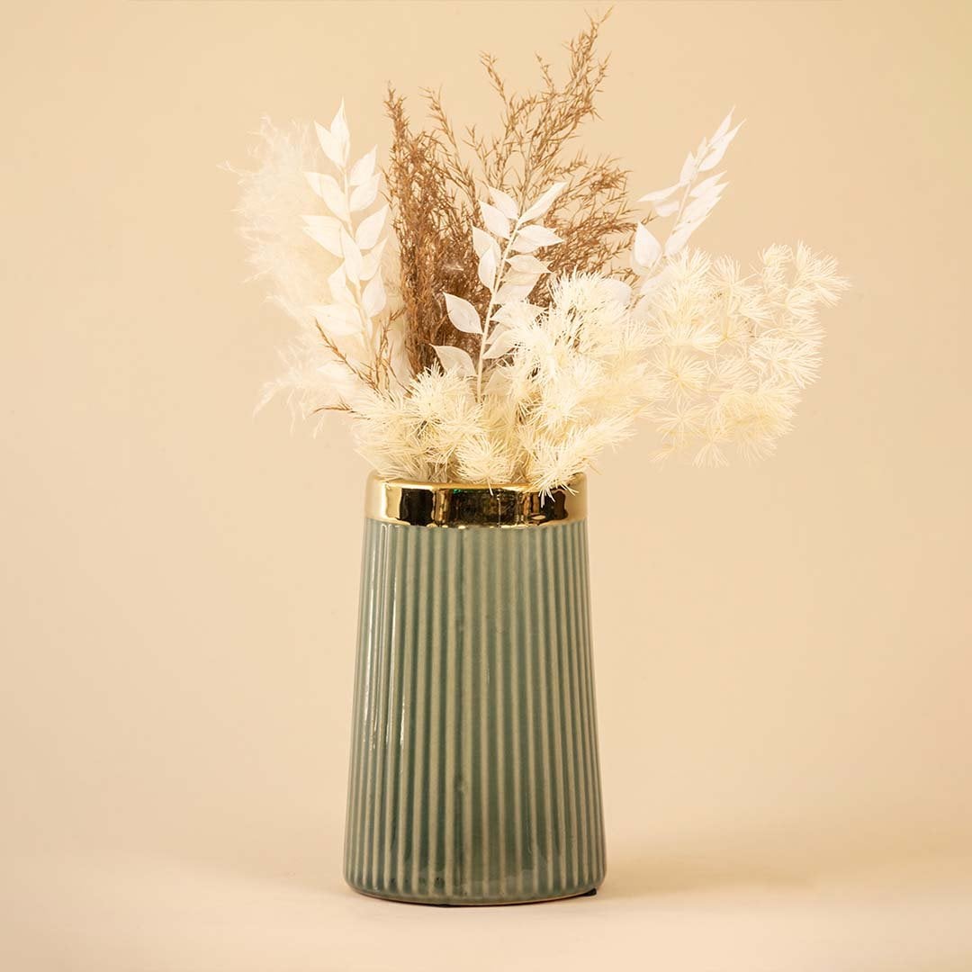 Elegant ribbed green ceramic vase with golden rim filled with soft white and beige dried flowers placed against a warm beige background for a sophisticated home decor look.