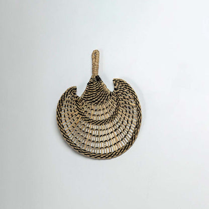 Side view of woven seagrass basket showing curved shape with rope handle and black striped pattern traditional construction.