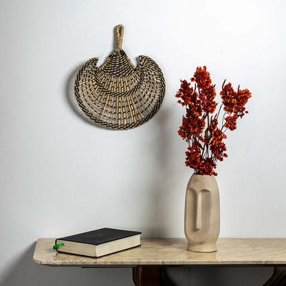 Black and natural woven seagrass decorative basket with handles displayed as bohemian handcrafted wall decor accent piece.