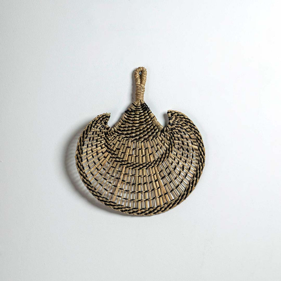 Round woven seagrass basket with black stripe pattern on white background showcasing handmade bohemian decorative wall piece.