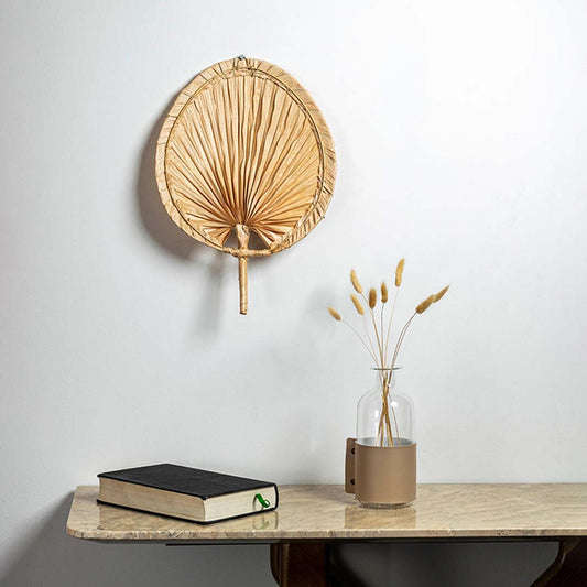 Natural woven palm leaf hand fan displayed on wall creating tropical bohemian handcrafted decor accent in home interior.