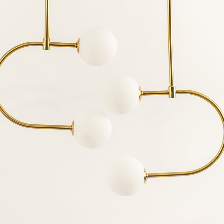 Modern ceiling chandelier light with curved gold rods holding four white globe shades arranged in a balanced flowing design against a light background.
