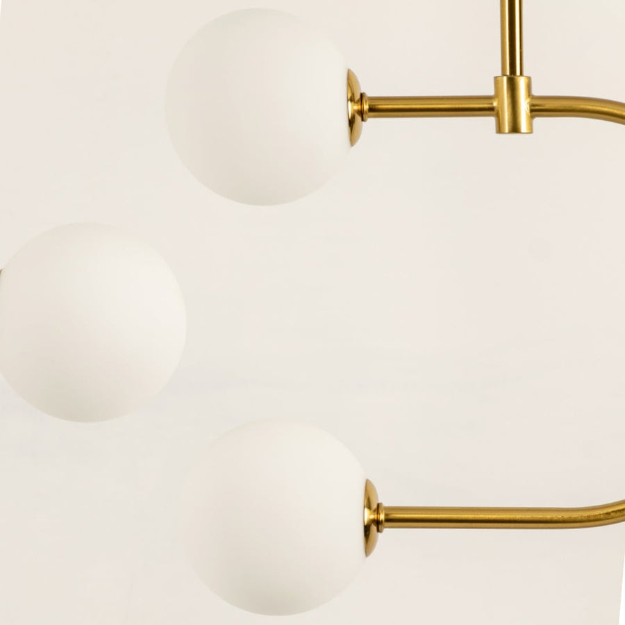 Close up of a modern ceiling chandelier light with gold rods supporting three round white frosted globes arranged in a smooth curved layout.