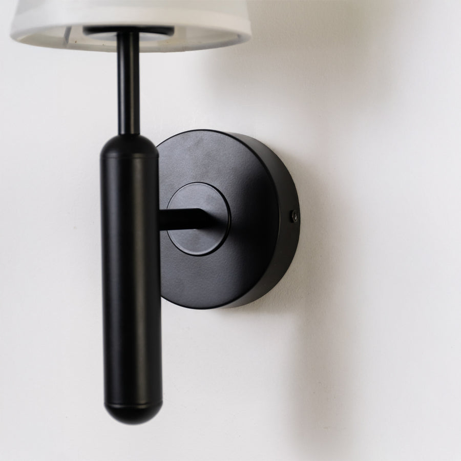 Minimal wall light in black metal finish with cylindrical arm for bedroom or living room decor lighting white background.