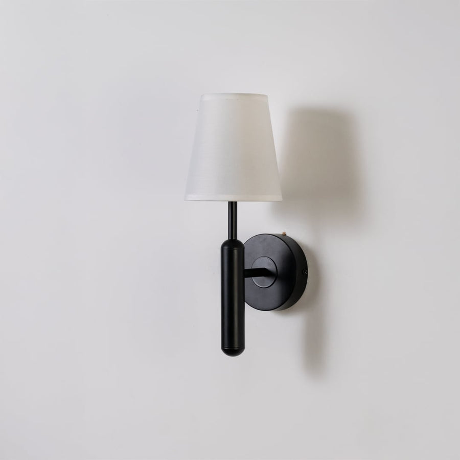 Black metal wall light with white fabric shade displayed on a white background with light off highlighting its sleek minimal contemporary form.
