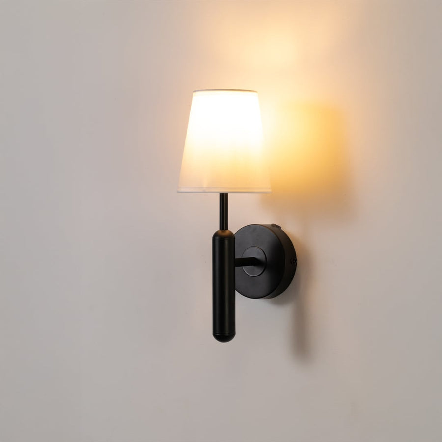 Black metal wall light with white fabric shade glowing softly on a clean white background ideal for bedroom hallway and living room modern lighting.