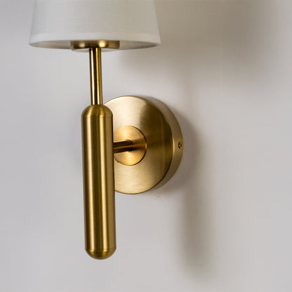 Modern wall light in gold metal finish with cylindrical arm for bedroom or living decor lighting placement white background.