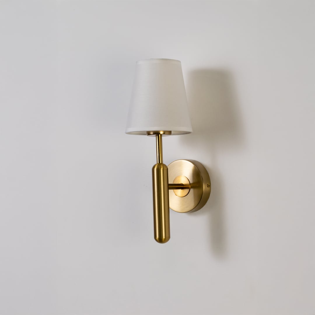 Gold metal wall light with white fabric shade displayed on a white background with light off highlighting its sleek minimal contemporary form.