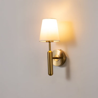 Gold metal wall light with white fabric shade glowing softly on a clean white background ideal for modern bedroom hallway and living room lighting.