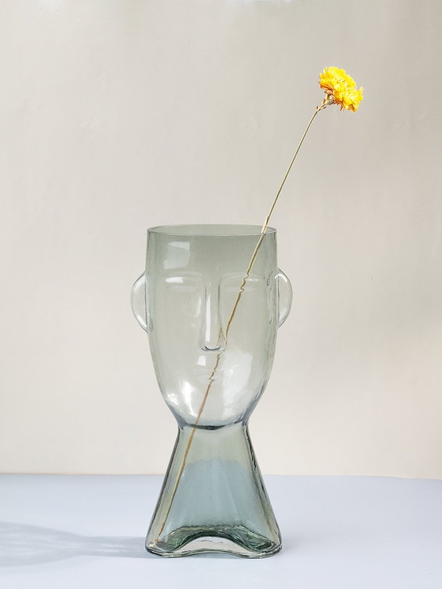 Clear glass vase in abstract human face shape tall decorative modern design light on white background for contemporary interiors.