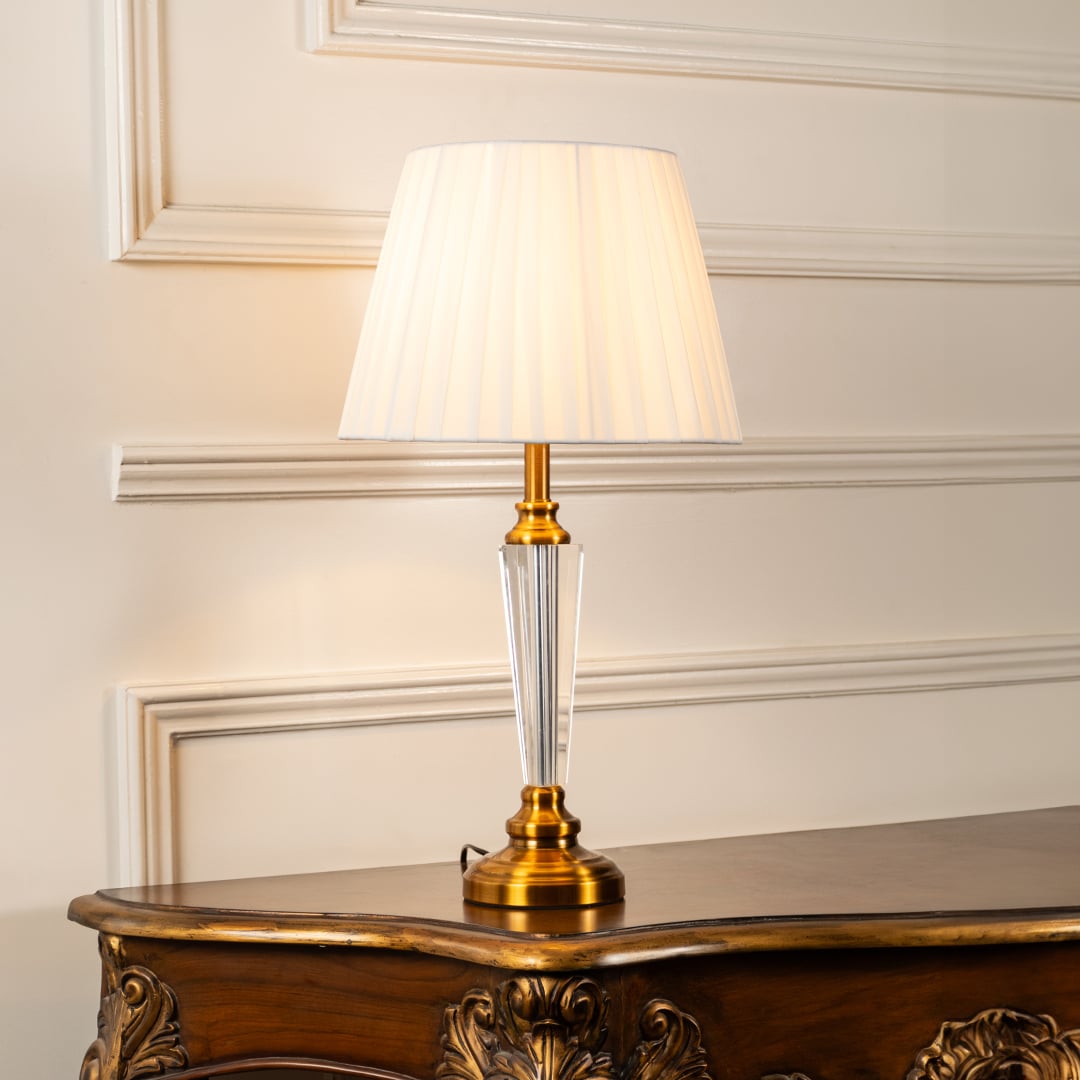Crystal and gold table lamp with pleated shade turned on against white background perfect for bedside table lamp.