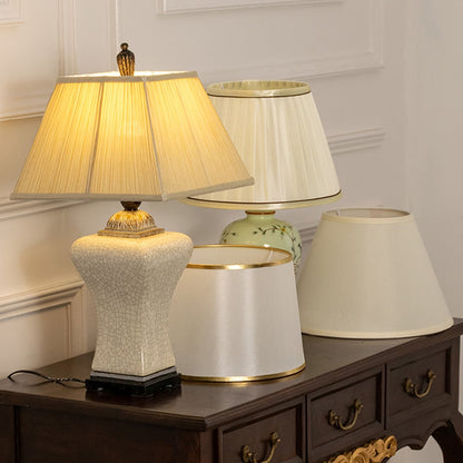 Pleated shade white ceramic table lamp on wooden sideboard with light on beside décor pieces for warm traditional décor.