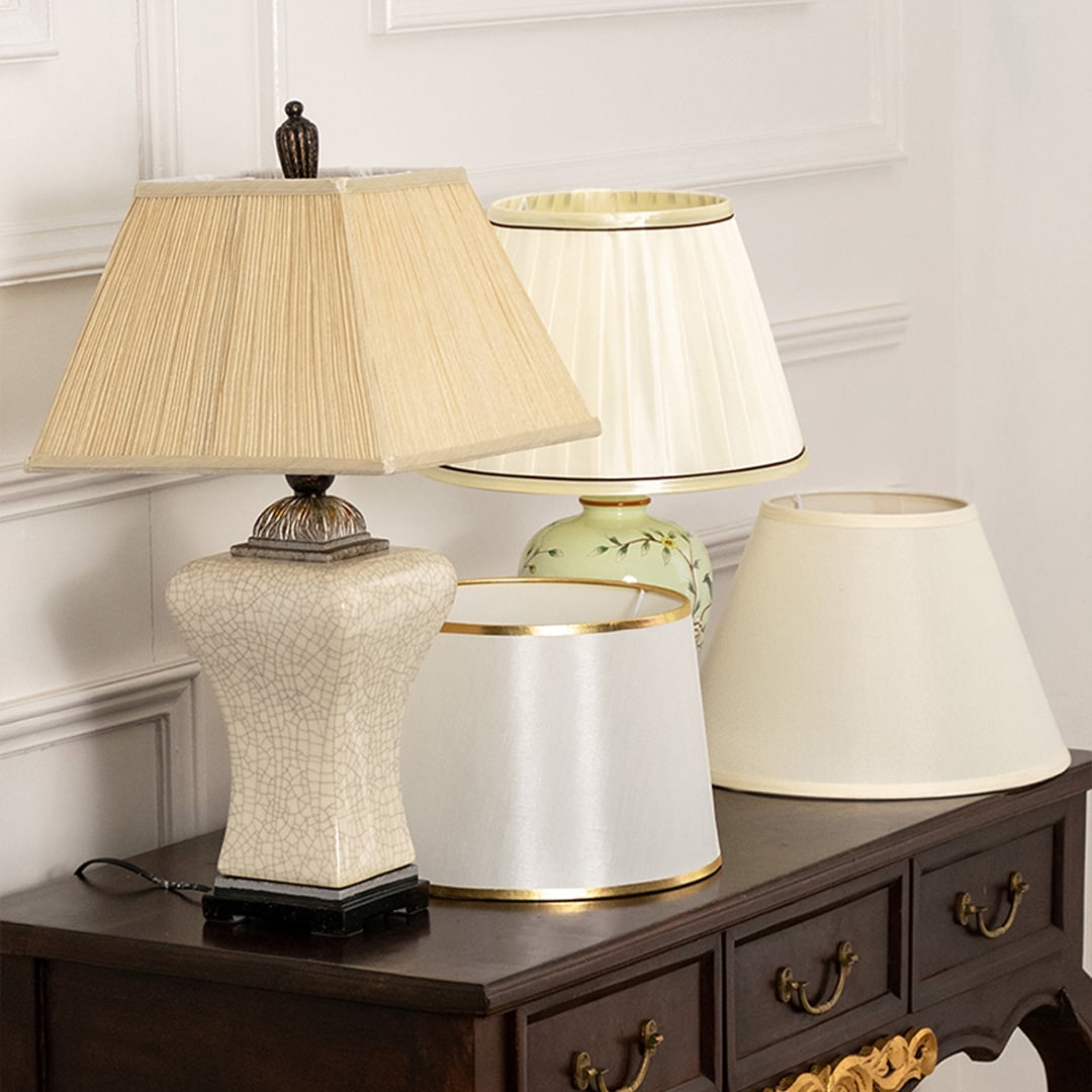 Pleated shade white ceramic table lamp on wooden sideboard with light on beside décor pieces for warm traditional home décor.