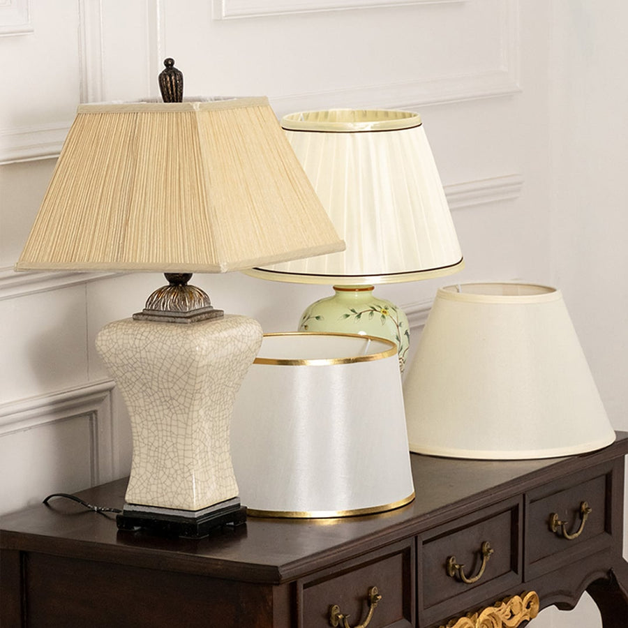 Pleated shade white ceramic table lamp on wooden sideboard with light on beside décor pieces for warm traditional home décor.