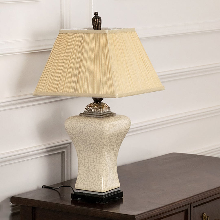 Pleated shade white ceramic table lamp on wooden sideboard with light on beside décor pieces for warm traditional home décor.