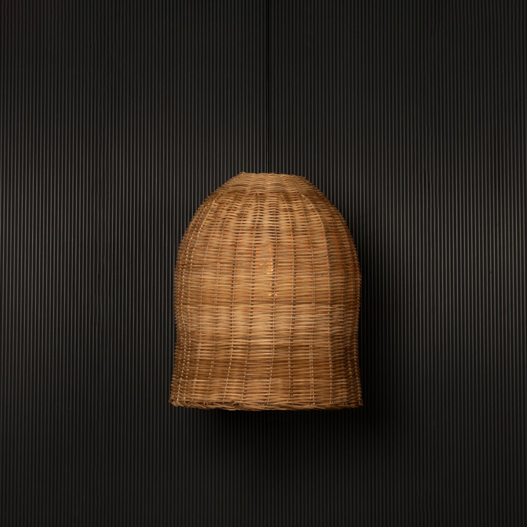 Dome-shaped rattan pendant light with handwoven bamboo shade turned on glowing softly against black background.